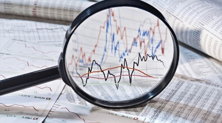 Magnifying glass over a heap of paper with graphs and tables